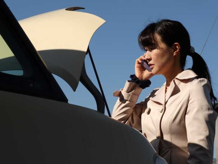 トランクが開いた車のそばで携帯電話をかける女性